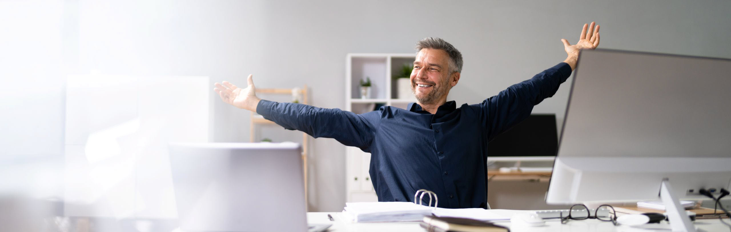 Entspannter Mann streckt die Arme im Büro aus – Symbol für effiziente Workflows, weniger Stress und einen erfolgreichen Arbeitstag da im A-NULL-Club